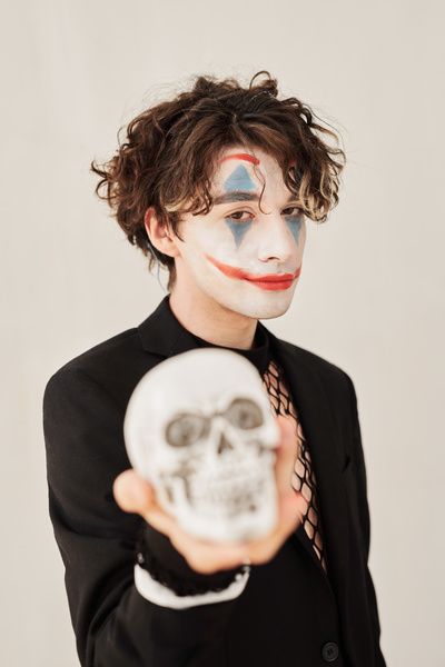 Man with Joker Makeup Stands on White Background and Holds Skull